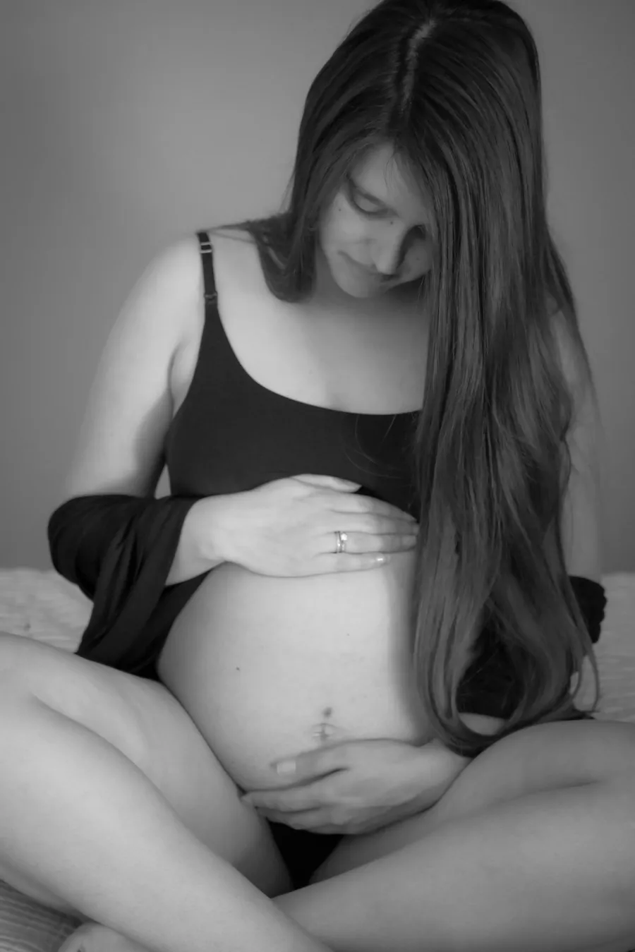Gravid kvinna sitter på sängen och håller om magen, behöver stöd för att sova bekvämt på sidan